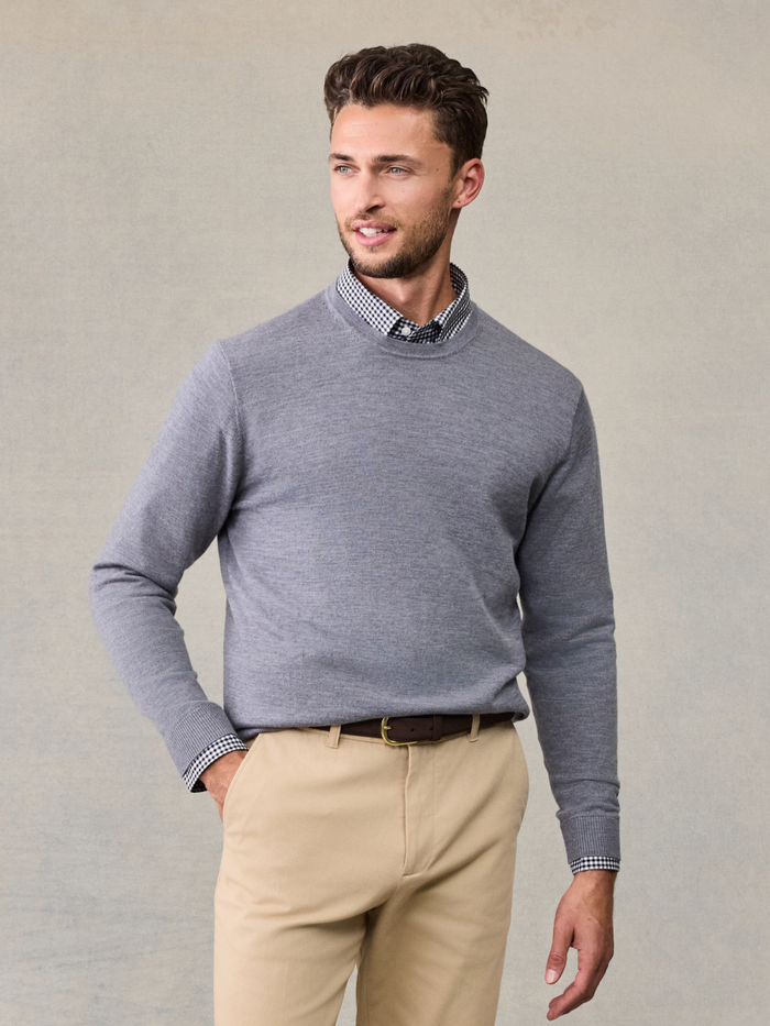 Man in heather grey crew sweater over checked collar shirt and khaki trousers