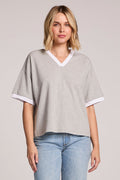 A front view of a woman making eye contact with the camera and wearing the Chaser Heather Grey Eden Tee on a neutral background