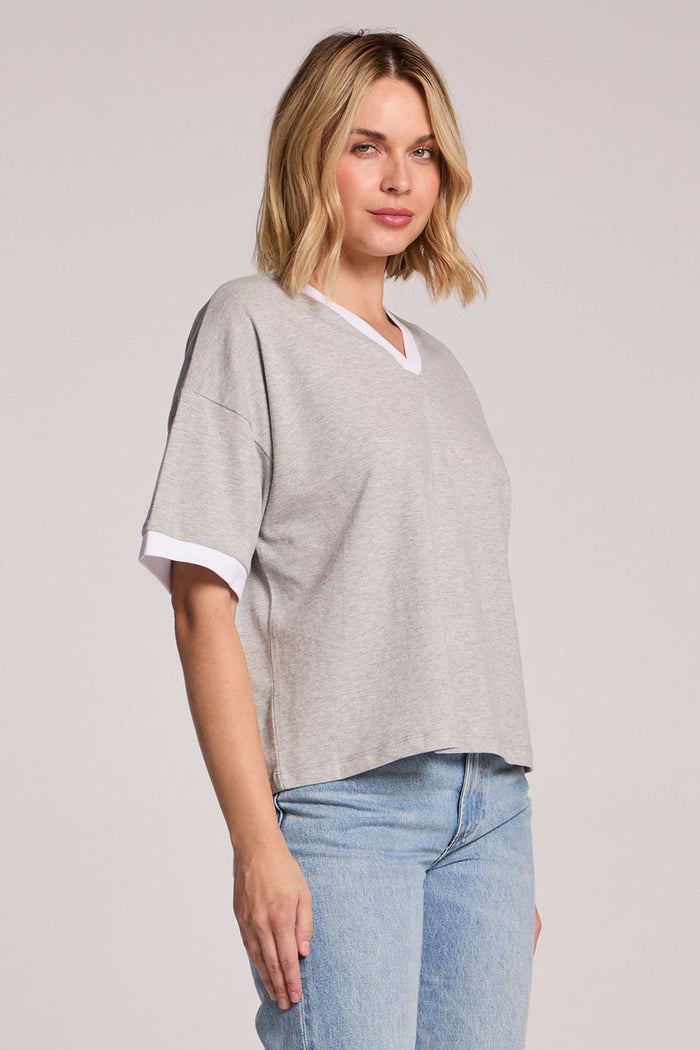 A side angle view of a woman wearing the Chaser Heather Grey Eden Tee and jeans on a neutral background