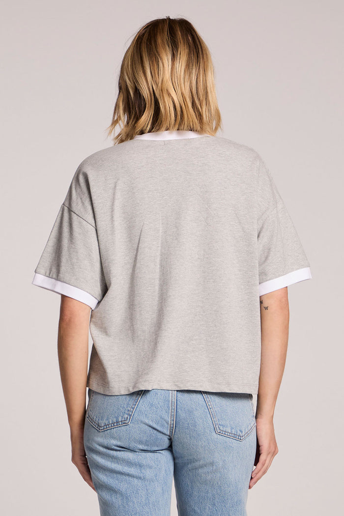 A back view of a woman wearing the Chaser Heather Grey Eden Tee on a neutral background