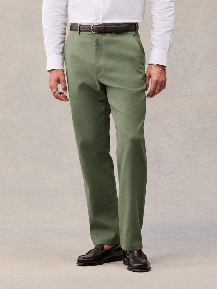 Dusty sage suit pants with a brown belt and black penny loafers, cropped waist-to-shoe view.