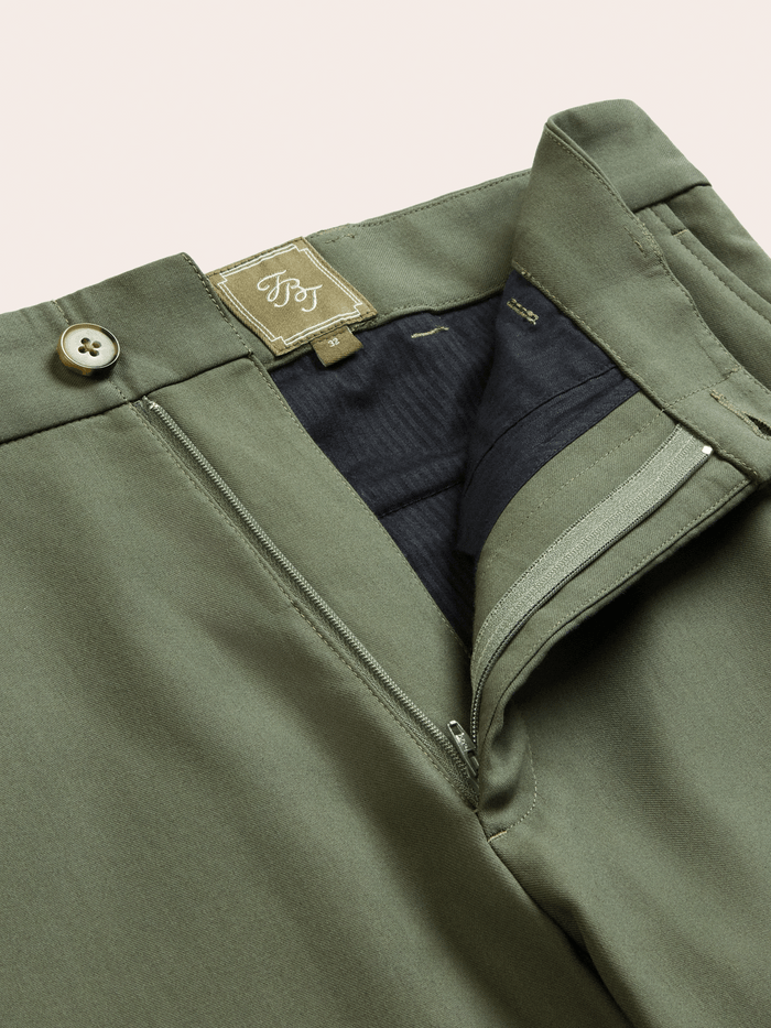 Dusty sage suit pants with the fly open, showing zip closure and interior brand label.