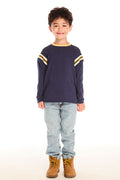 Full body view of boy wearing Chaser’s I Am #1 navy long sleeve top with yellow stripes, light blue jeans, and brown boots on a white background