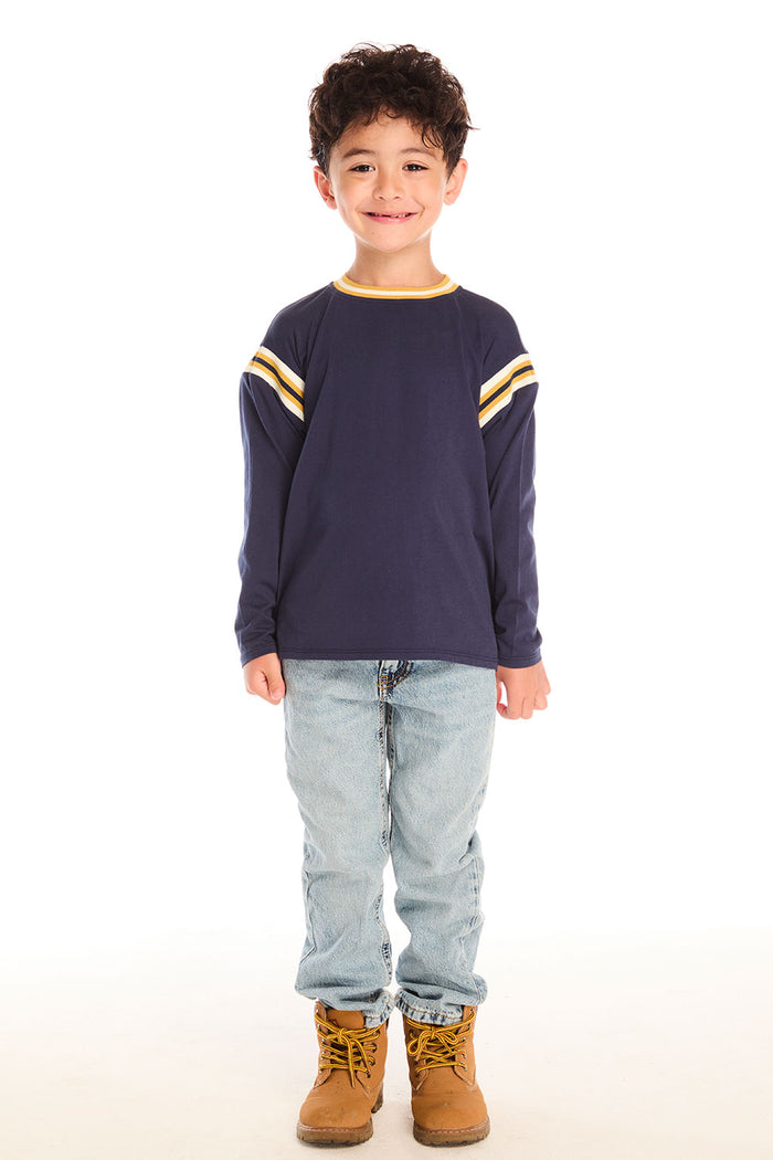 Full body view of boy wearing Chaser’s I Am #1 navy long sleeve top with yellow stripes, light blue jeans, and brown boots on a white background