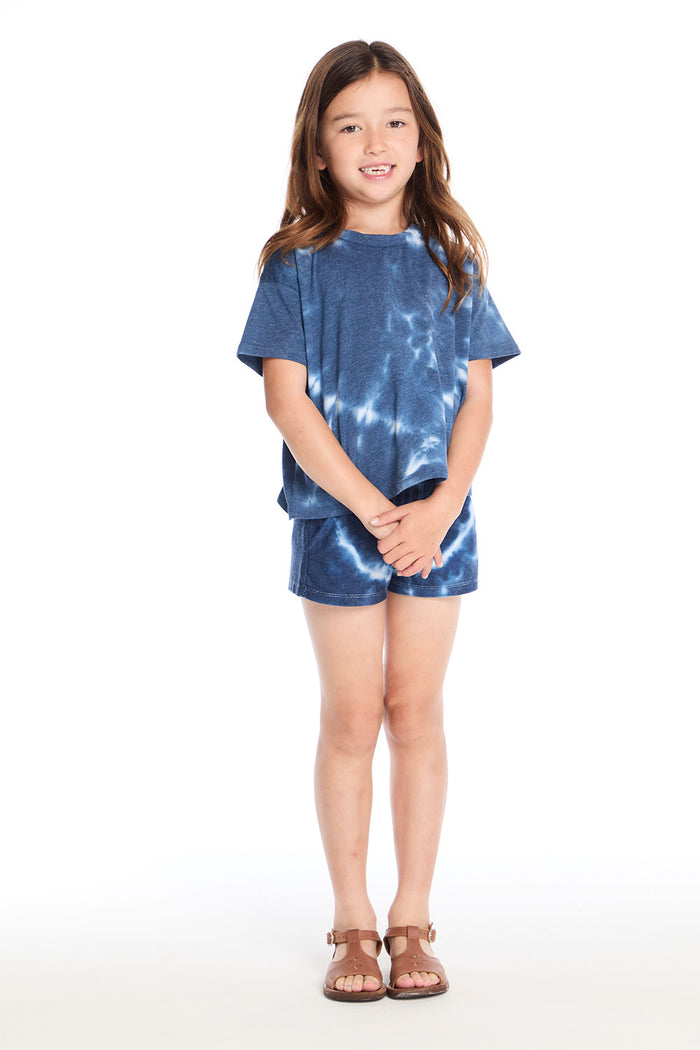 Girl wearing the Chaser Kids Indigo Heart Tie-Dye T-Shirt with matching Jade Indigo Heart Shorts and brown sandals on a white background