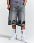 Person wearing gray denim shorts with black designs and white sneakers on a white background