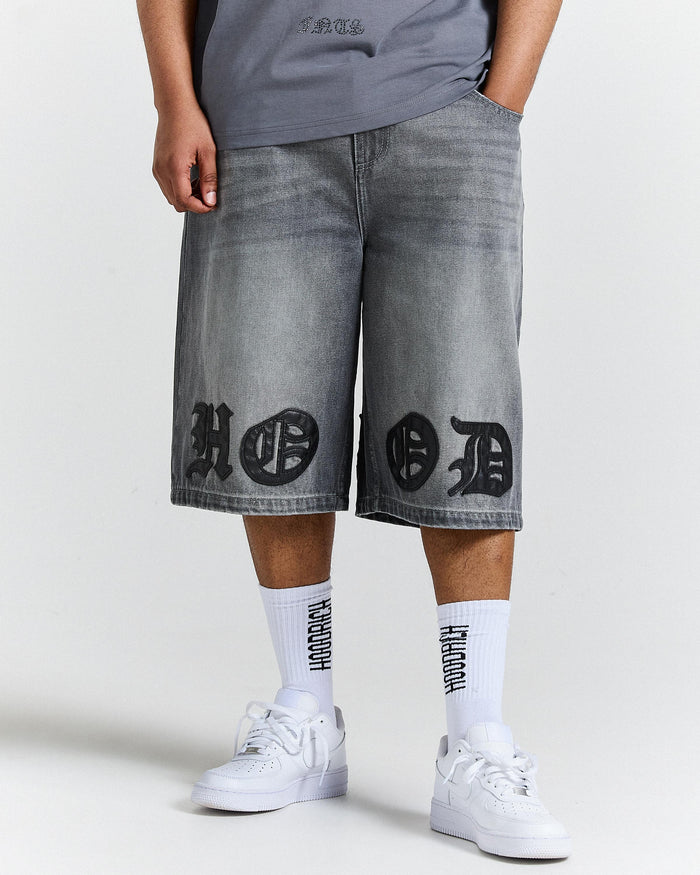Person wearing gray denim shorts with black designs and white sneakers on a white background
