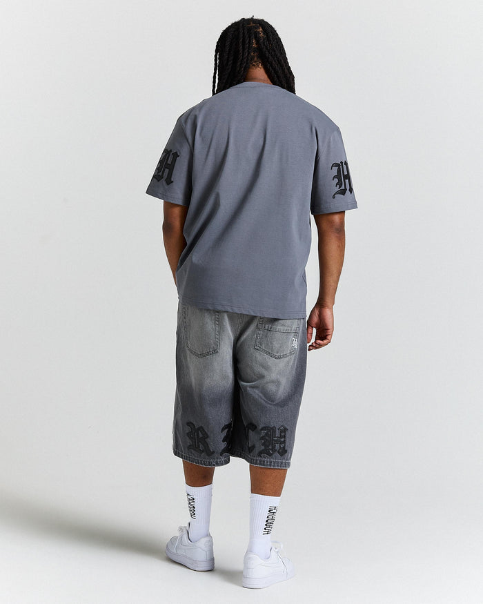 Person wearing a gray t-shirt and denim shorts with branding on a white background