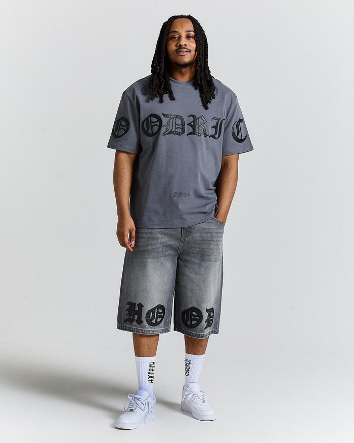 Person wearing a gray t-shirt and denim shorts with branding on a white background