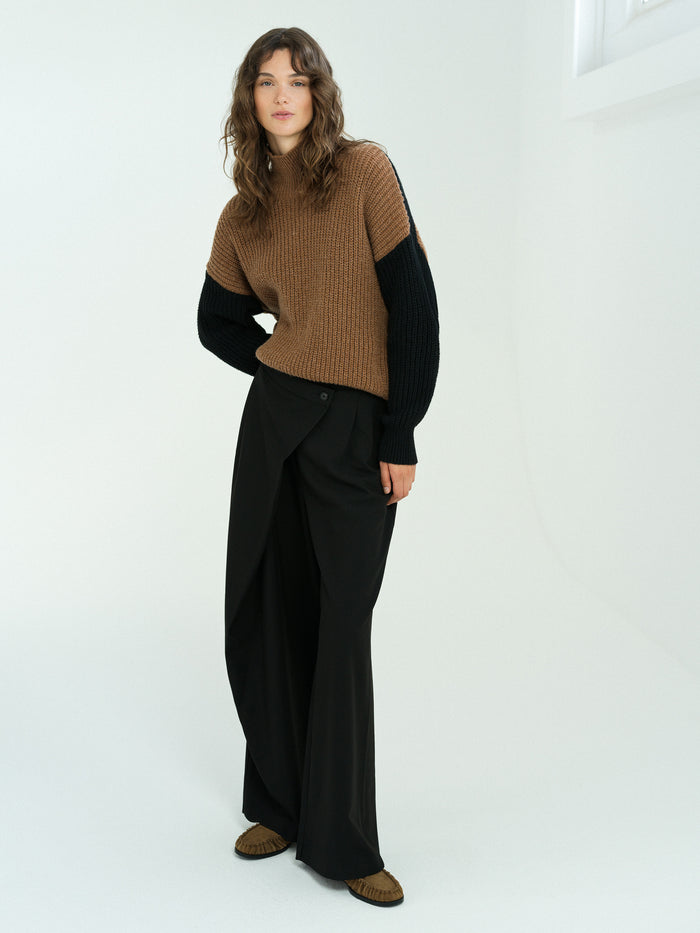 A woman wearing a brown and black textured knit jumper with a relaxed fit, ribbed roll neck and long sleeves.