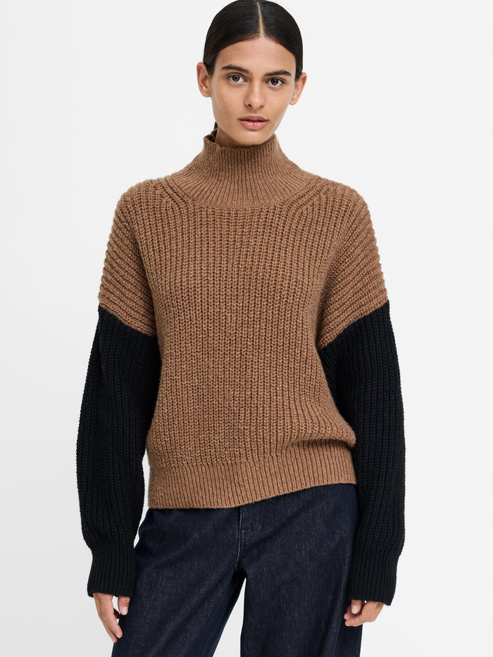A woman wearing a brown and black textured knit jumper with a relaxed fit, ribbed roll neck and long sleeves.