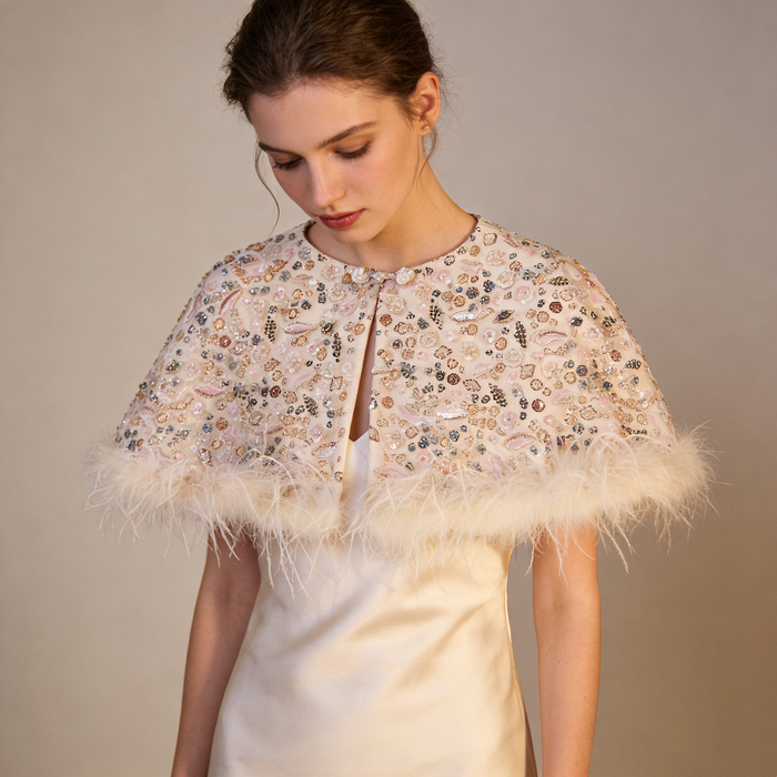 Elegant ivory wedding cape with sparkling beadwork and soft feather edge, romantic bridal shoulder cover for ceremony.