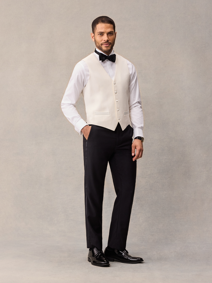 Man in ivory tuxedo vest, black bow tie, and black trousers, full-length front view