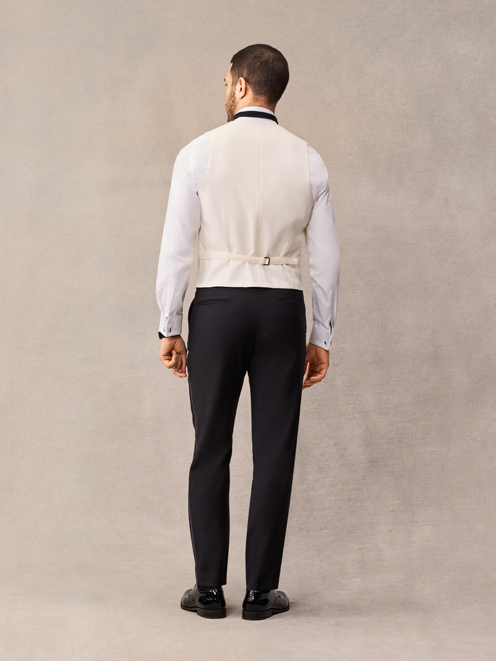 Back view of man in ivory tuxedo vest with strap buckle over black trousers