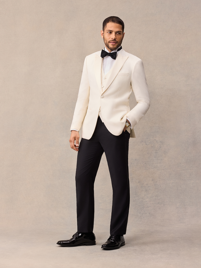 Man in ivory dinner jacket with peak lapel, black bow tie, and black trousers