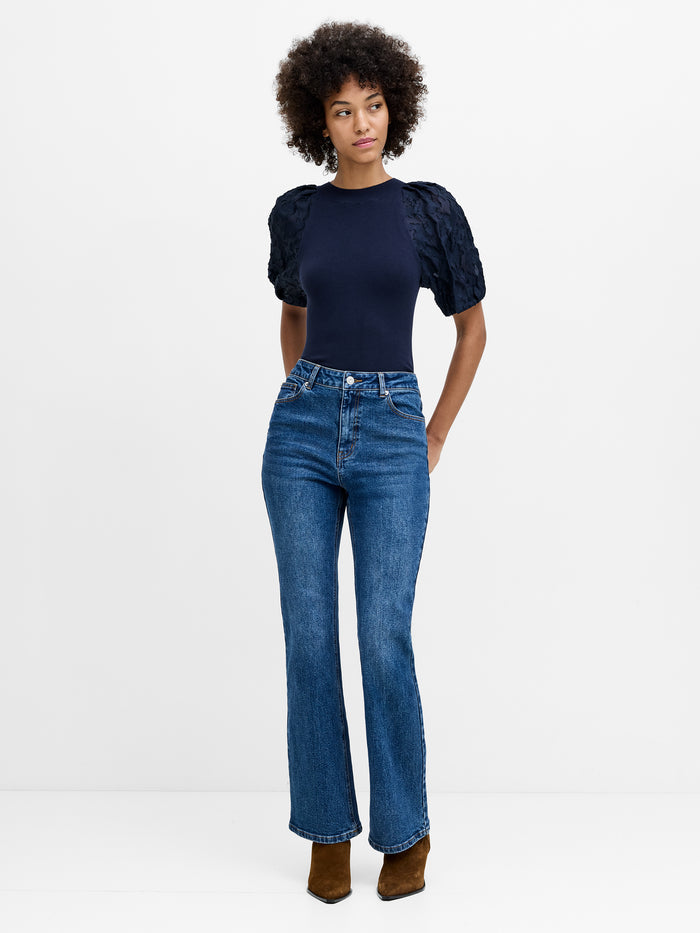 A woman wearing full length high waisted blue jeans with a fly zip and bootcut fit.