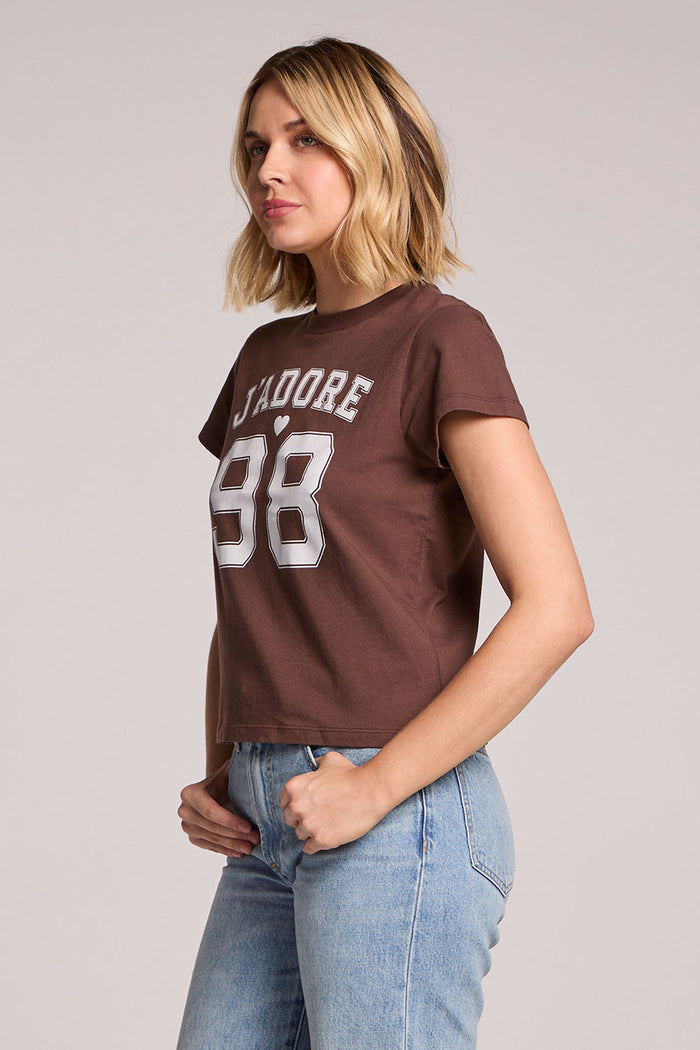 Side angle view of a woman wearing the Chaser J'adore 98 Tee on a neutral background with her hands in her pockets