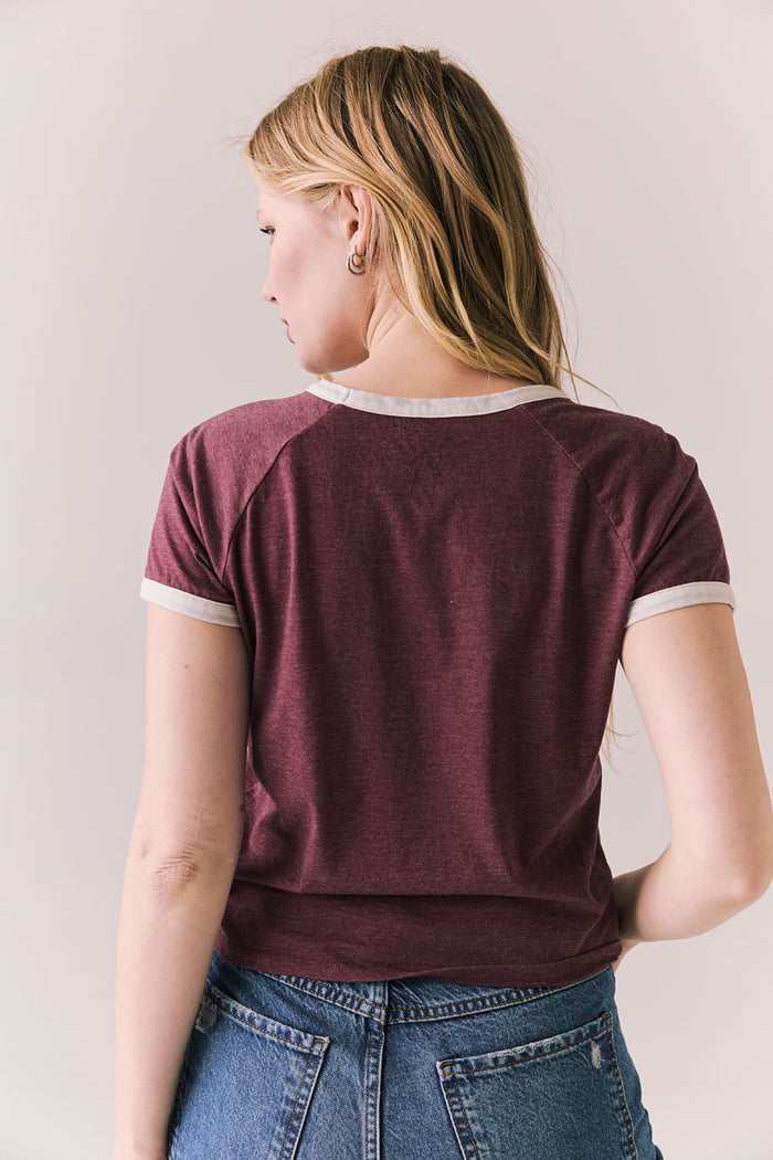 Back view of model in J’adore Vinyl Tee in fig purple with cream ringer trim and vintage-style text