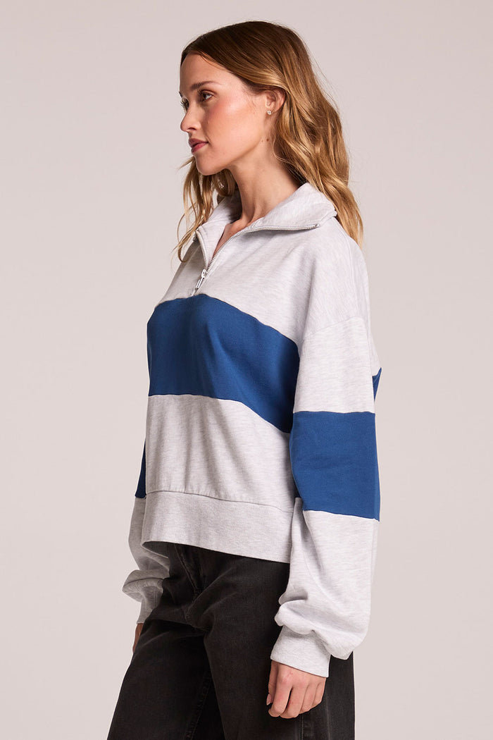 Side view of a woman wearing the Chaser  Jaime Admiral and Grey Half Zip on a neutral background with arms at her sides