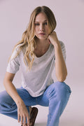 Full body crouching view of Chaser Brand Jameson Light Heather Grey Tee paired with jeans and slides in a relaxed pose