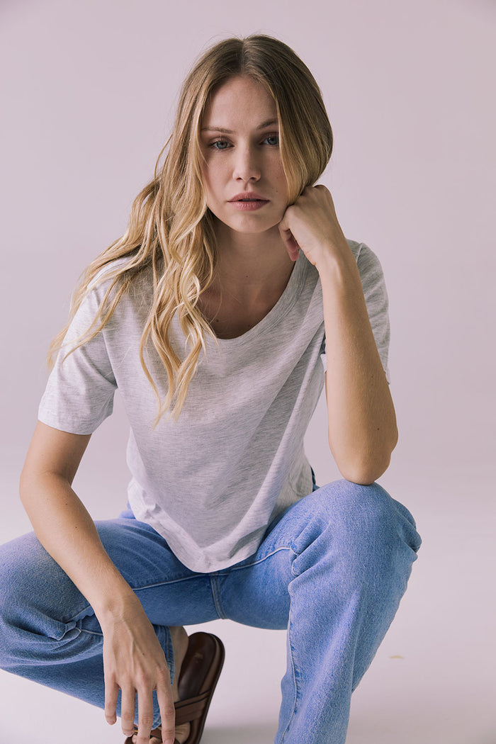 Full body crouching view of Chaser Brand Jameson Light Heather Grey Tee paired with jeans and slides in a relaxed pose