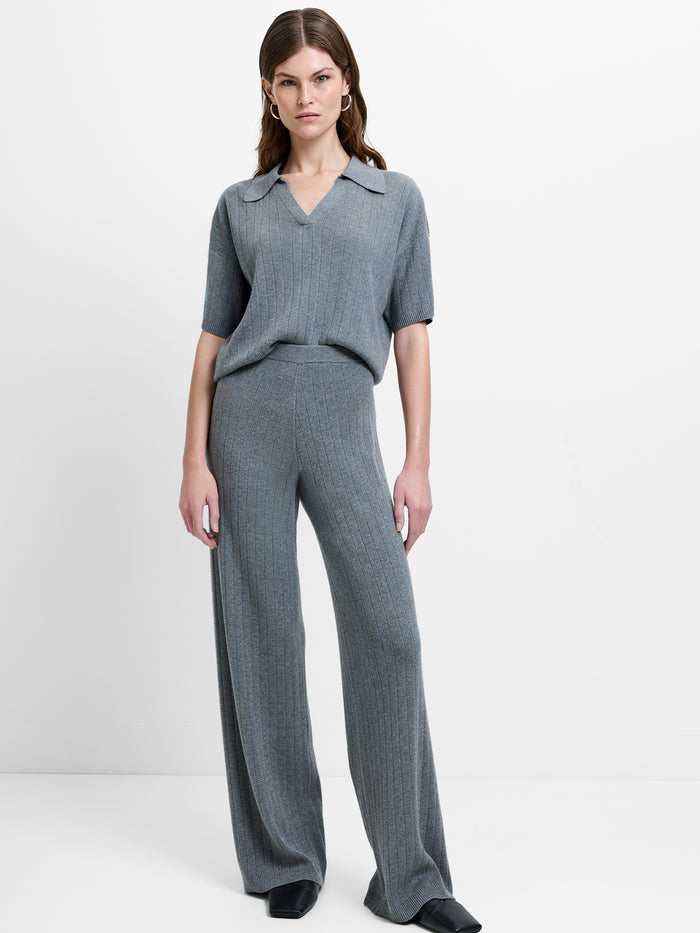 Woman wearing a soft knit, ribbed grey co-ord, featuring a short sleeve polo top with wide leg relaxed trousers with an elasticated waistband
