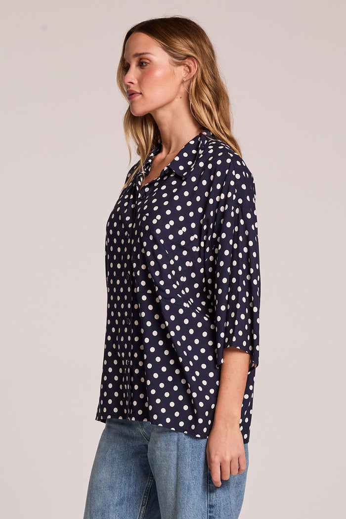Side angle view of a woman wearing the Chaser Jemma Navy Spot Button Down on a neutral background with arms at her sides