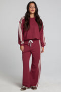 A full body front view of a woman wearing the Chaser Jessee Brick Red Trackpants on a neutral background