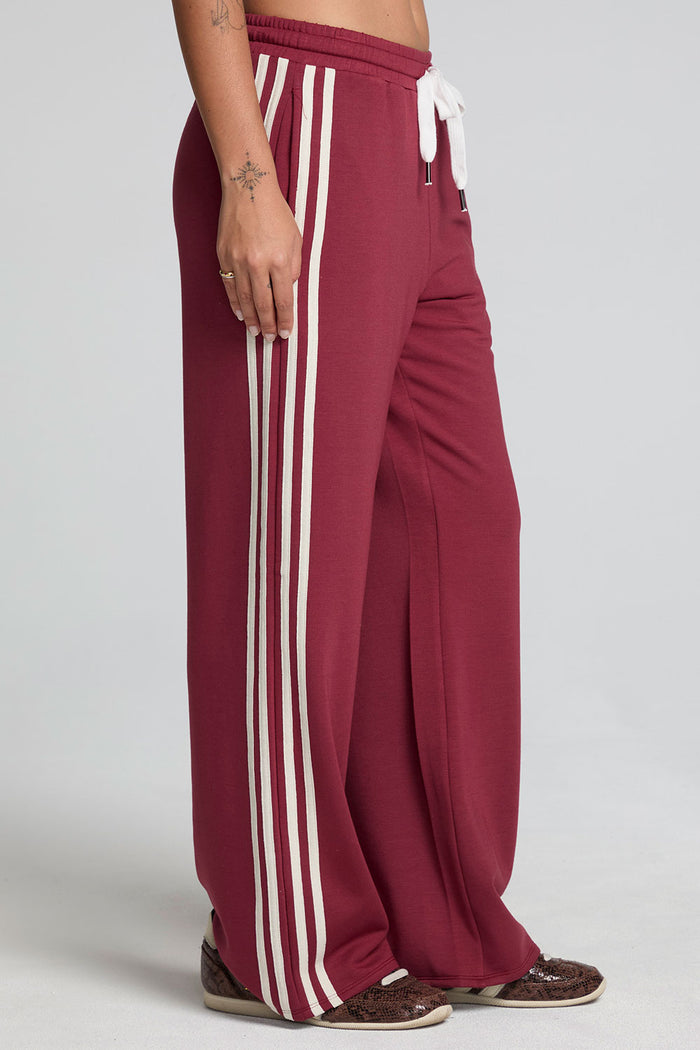 Side angle view of a woman wearing the Chaser Jessee Brick Red Trackpants on a neutral background with arms lowered at sides
