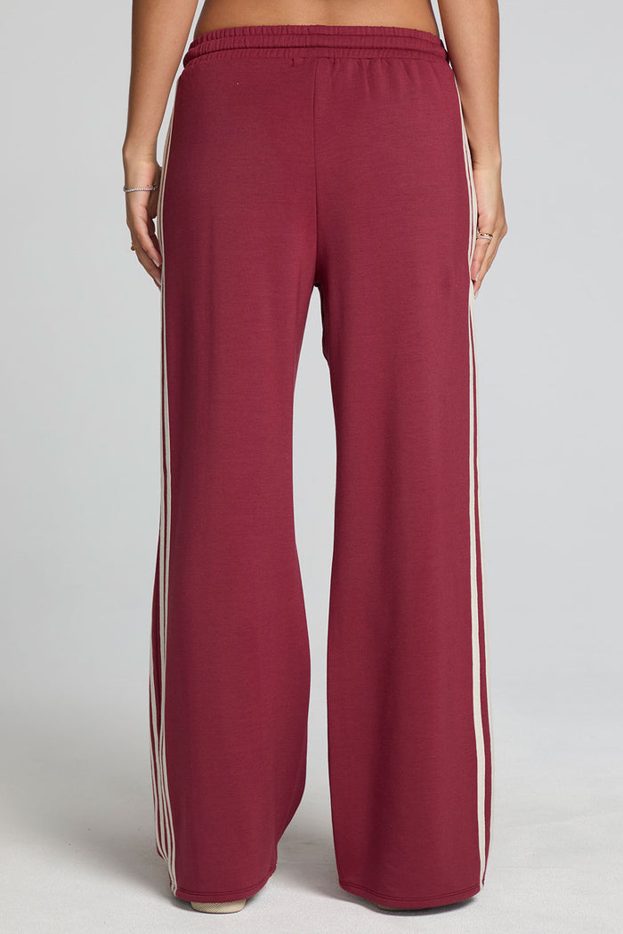 Back view of a woman wearing the Chaser Jessee Brick Red Trackpants on a neutral background with arms at sides