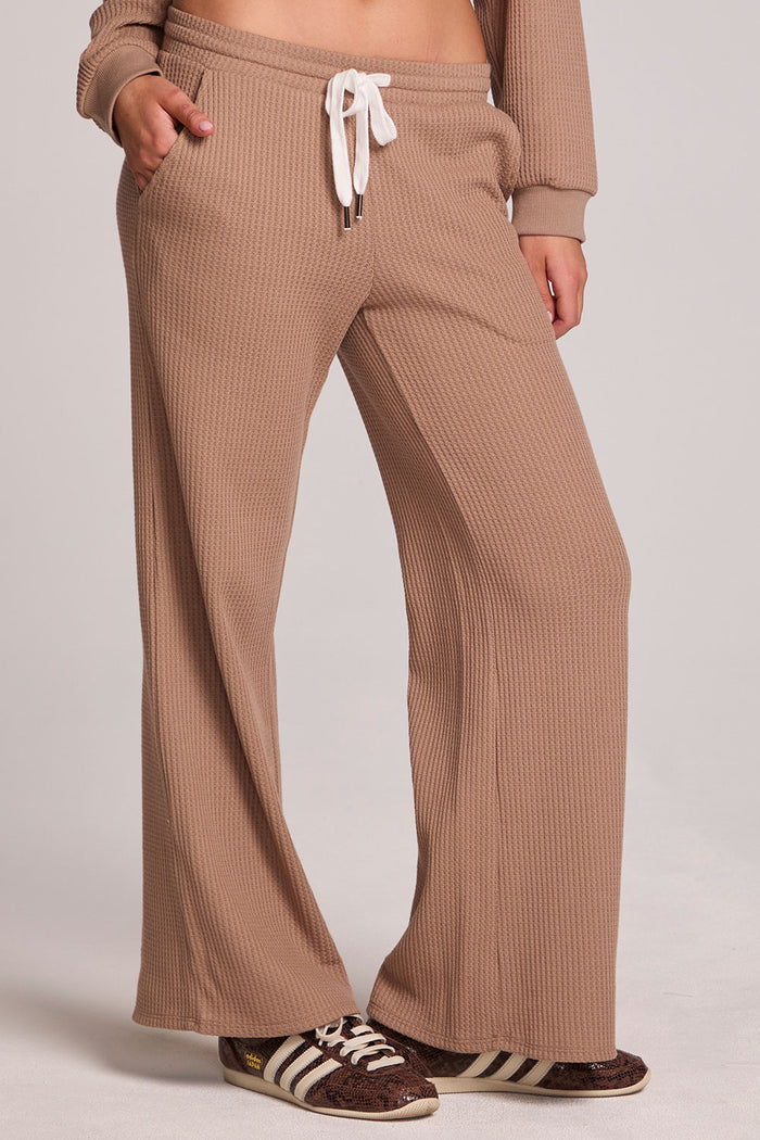 Front view of a woman wearing the Chaser Jorgia Camel Pants on a neutral background with shoes and hands in pocket
