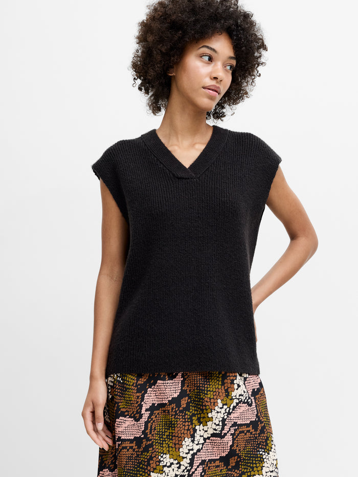 A woman wearing a dark grey knit vest with a v-neckline, cap sleeves and a relaxed fit.
