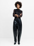 A woman wearing full length black PU Trousers with a high waistband, 2 side pockets, hook and zip fastening and a barrel fit.