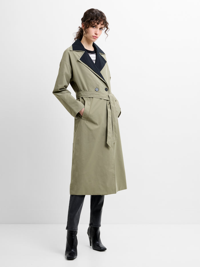 Woman wearing a khaki green belted trench coat with a black collar