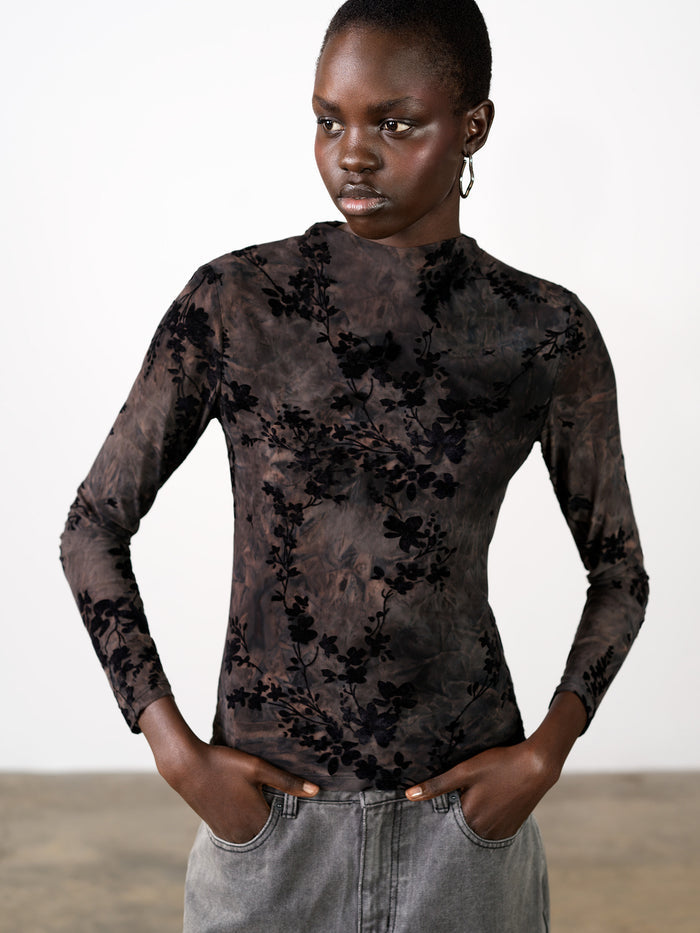 A woman wearing a black and brown fitted top with long sleeves, a mock neck and a floral velvet pattern.