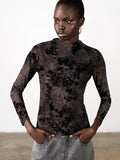 A woman wearing a black and brown fitted top with long sleeves, a mock neck and a floral velvet pattern.