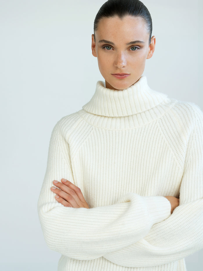 A woman wearing a cream funnel neck knit jumper with long sleeves, a regular fit and a ribbed hem.