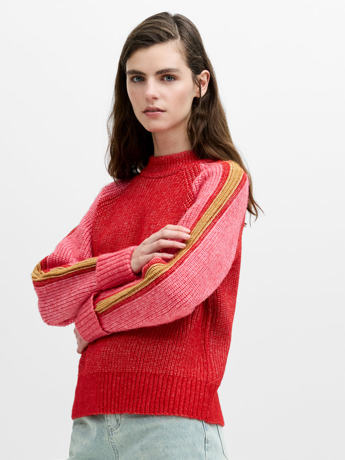 A woman wearing a red knit jumper with pink and yellow striped raglan sleeves and a ribbed mock neck.