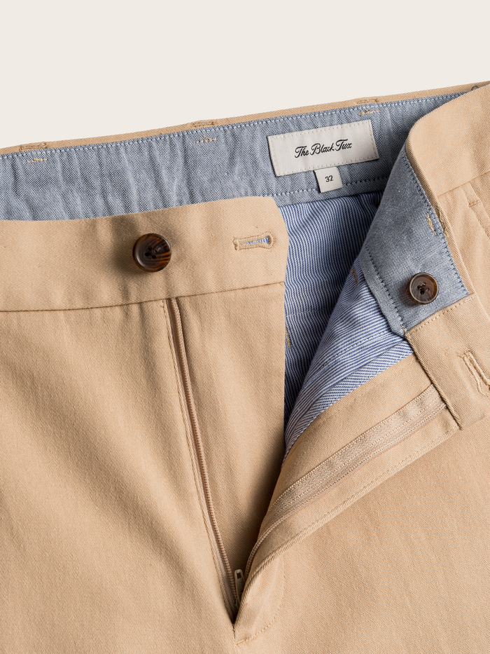 Close-up of khaki chino trousers waistband, brand label, and open fly