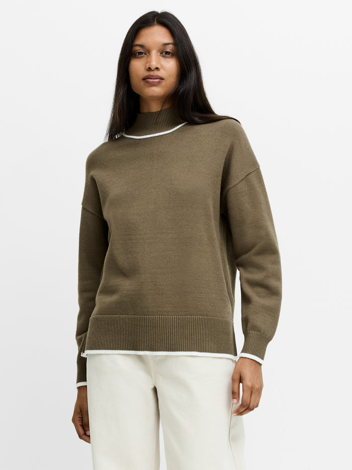 A woman wearing a knit khaki green and white Jumper with dropped shoulders, long sleeves, a ribbed mock neck, contrasting trim and a relaxed fit.