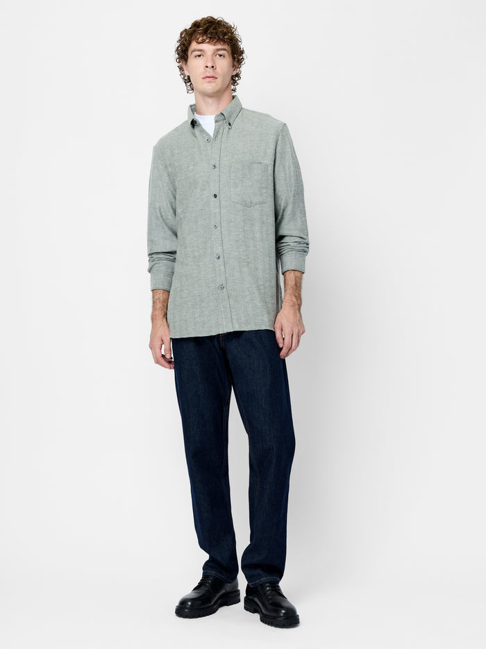 A man wearing a khaki green and grey shirt with long sleeves, a pointed collar and button down fastening.