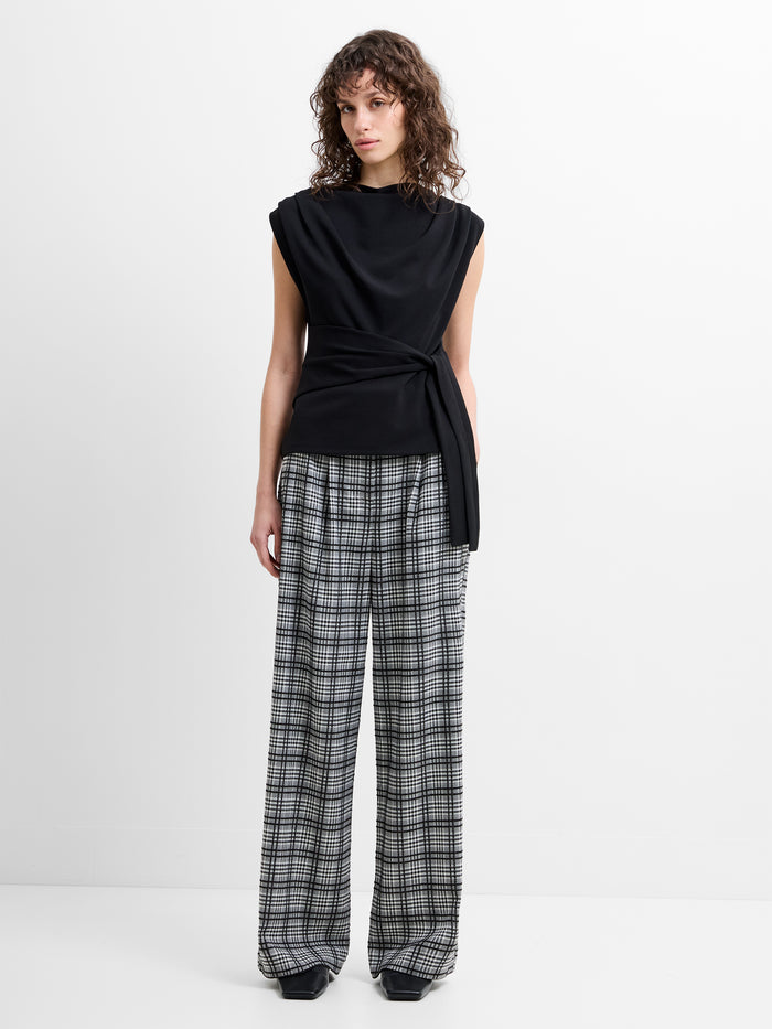 Woman wearing a black sleeveless top and grey and black check wide leg pleated trousers