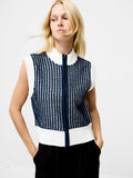 A woman wearing a knitted sleeveless zip up jumper with a full length metal zip, a white and dark blue lattice stitch and a white high neckline.