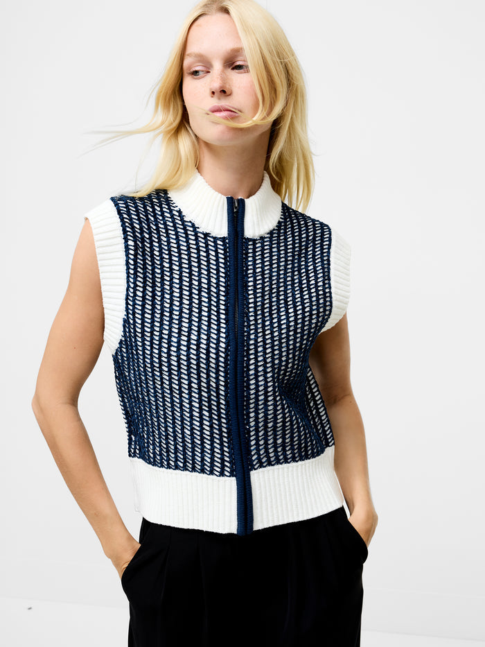 A woman wearing a knitted sleeveless zip up jumper with a full length metal zip, a white and dark blue lattice stitch and a white high neckline.