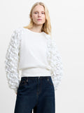 Woman wearing a white long sleeve knitted jumper with ruffled sleeves