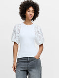 A woman wearing a white knit top with sheer puff sleeves, a crew neckline and a ribbed hem.