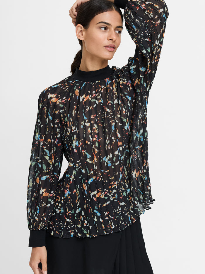 A woman wearing a relaxed fit semi-sheer black blouse with long sleeves, a multi-colored abstract print and high neckline.