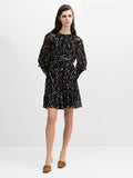 A woman wearing a black mini dress with an abstract print and ruffle detailing,  long puff sleeves, a tie waist and a round neckline.