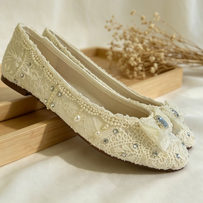 Bride wearing elegant lace wedding flats with crystal bows under a flowing bridal gown during a romantic wedding photoshoot.