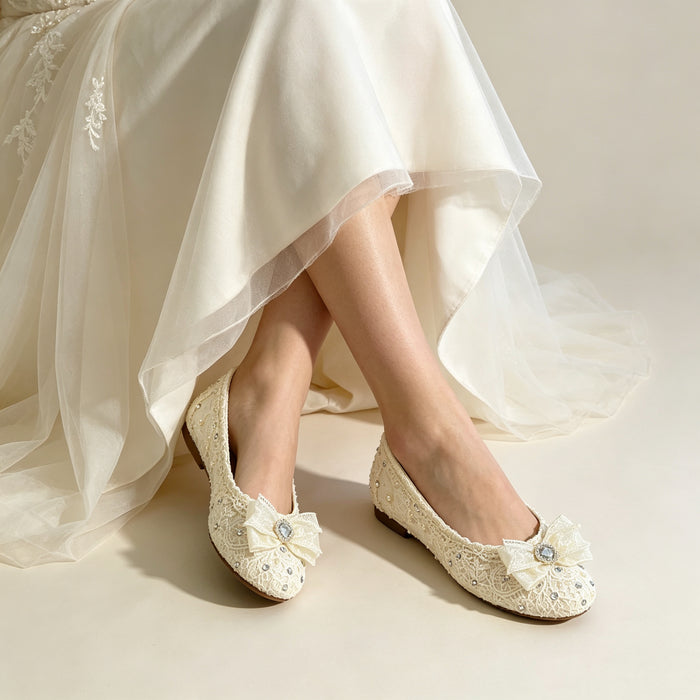 Bride wearing elegant lace wedding flats with crystal bows under a flowing bridal gown during a romantic wedding photoshoot.